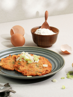 korean kimchi pancakes on a plate with flour eggs and garlic in the background.