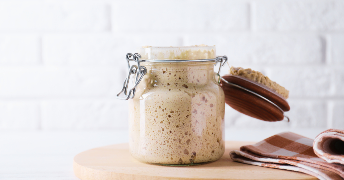 image of sourdough starter in a glass jar sitting on a wooden table.
