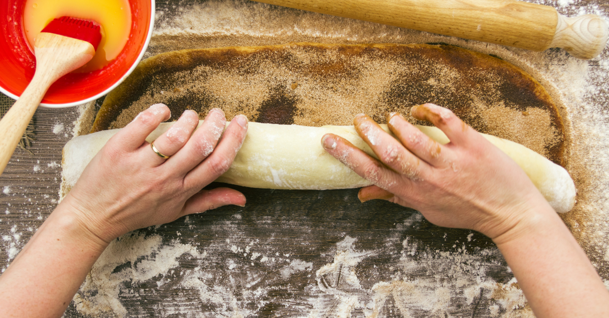 image of woman hands rolling up cinnamon roll dough on a wooden table.