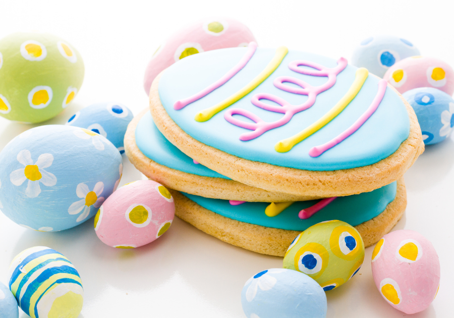 image of decorated egg shaped sugar cookies laying on a white background with colorful decorated easter eggs surrounding the cookies.