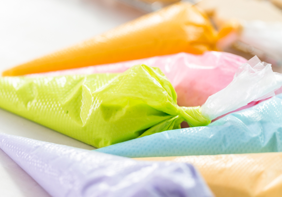 image of colorful royal icing in piping bags laying on a white table.